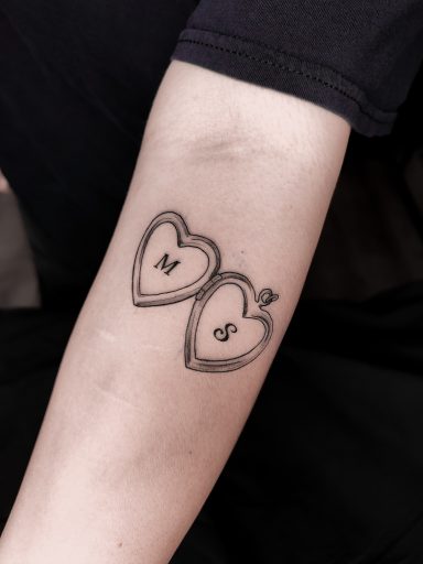 fineline heart medallion tattoo with letters / writing on forearm, done in Lörrach